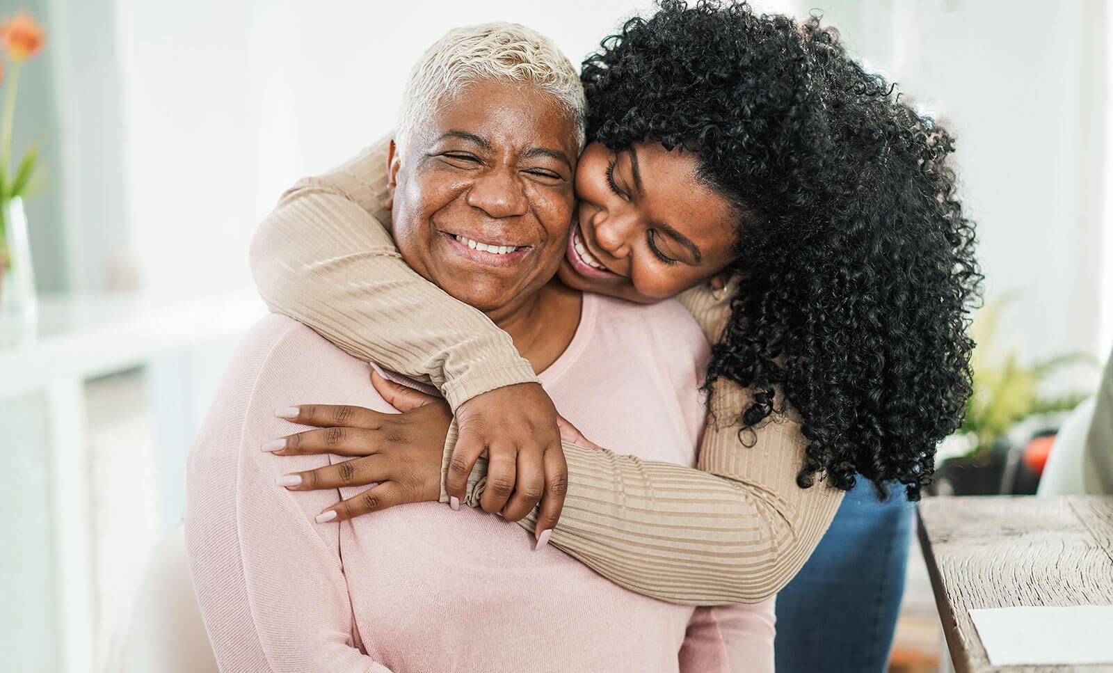 Daughter smiling and hugging her mother from behind.
