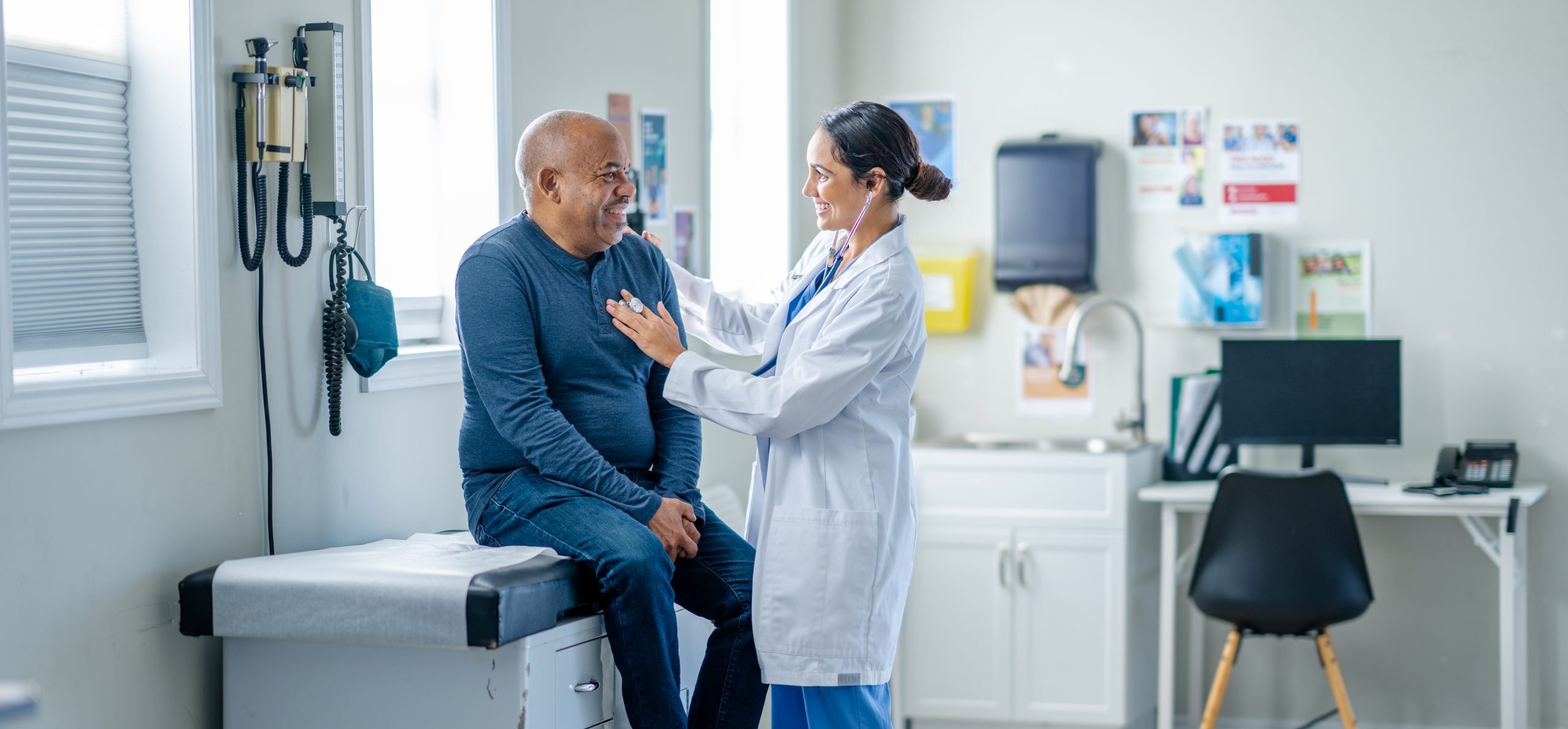 Female doctor wearing a stethoscope and listening to the the chest of her male patient.