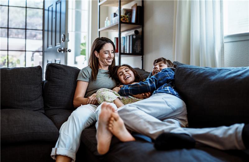Mother and laughing children cuddling on a couch.